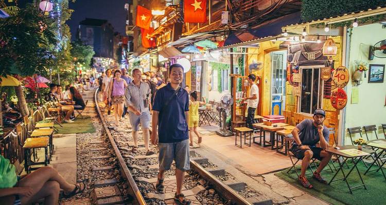 Personas paseando por una vía férrea bordeada de cafés por la noche.