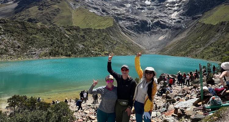 Drei Personen posieren vor einem türkisfarbenen See mit Bergen im Hintergrund