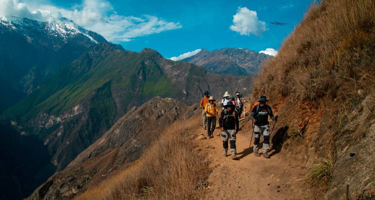 Excursionistas en un sendero accidentado con montañas al fondo.