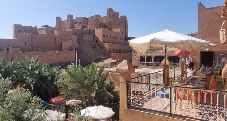 Restaurante con terraza al aire libre con vistas a un complejo de kasbah de tierra fortificada en el desierto.