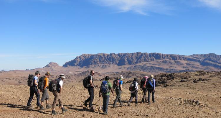 Grupo de trekistas caminando a través de una meseta árida con montañas escarpadas a lo lejos.