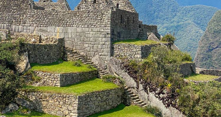 Ruines de pierre avec des marches en pierre entourées de montagnes vertes.