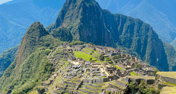 Vue des ruines de Machu Picchu depuis les hauteurs avec des montagnes vertes en arrière-plan.
