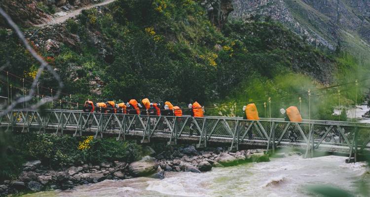 Excursionistas con mochilas cruzando un puente sobre un río.