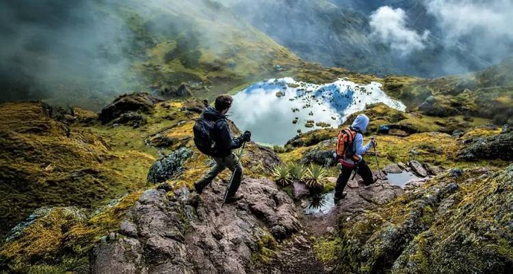Excursionistas descendiendo una montaña con vista a un lago.