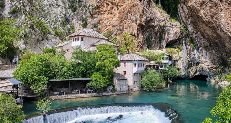 Image claire d'une rivière coulant à travers un paysage rocheux avec des bâtiments historiques à Blagaj, Bosnie.