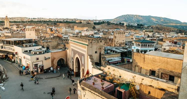 Vista elevada sobre la medina antigua de Fez con la ornamentada Puerta Azul y colinas distantes bajo cielos despejados.