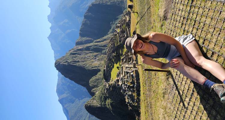 Femme souriante assise avec une vue panoramique du Machu Picchu en arrière-plan.