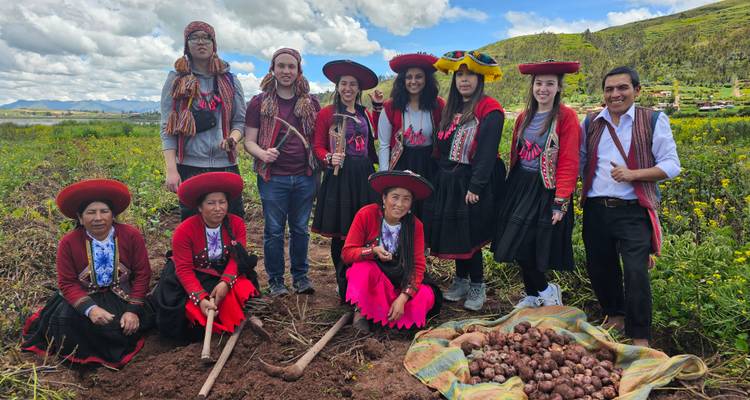 Groep mensen in traditionele kleding die landbouwgereedschap vasthoudt in een landelijke omgeving.