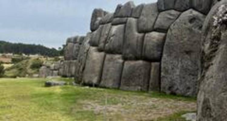 Haut mur de pierre avec des pierres bien ajustées dans une zone herbeuse ouverte.