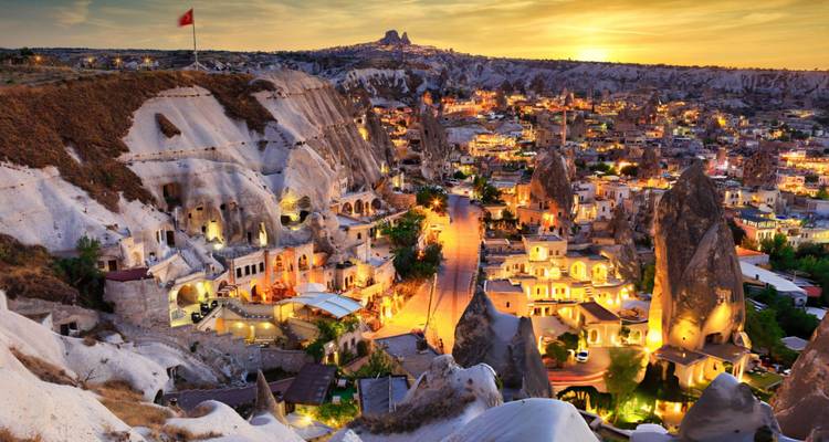 Vue du paysage rocheux de la Cappadoce avec des formations rocheuses uniques et des bâtiments illuminés au crépuscule.