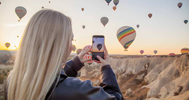 Femme photographiant des montgolfières au lever du soleil au-dessus de la Cappadoce.