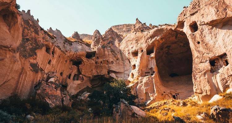 Formations rocheuses et grottes de couleur orange de la Cappadoce sous un ciel lumineux.