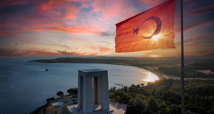 Drapeau turc au coucher du soleil au-dessus d'un monument et du littoral de la mer Égée.