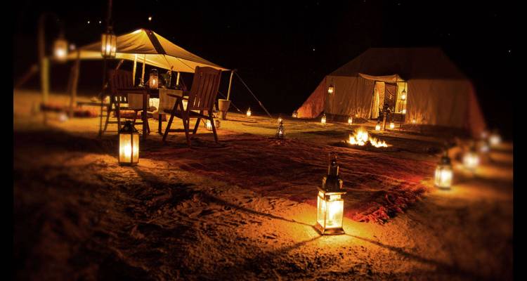 Vue nocturne d'un campement désertique avec des tentes et des lanternes.