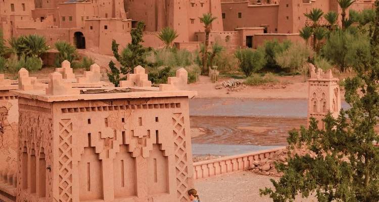 Erdbrücke und befestigte Lehmziegelmauern von Ait Benhaddou neben einem flachen Fluss in Marokko.