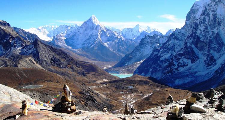 Vue imprenable sur les montagnes enneigées et le lac cristallin avec des cairns au premier plan.