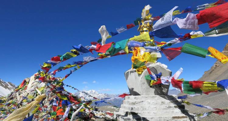 Coloridas banderas de oración colgadas sobre un monumento de piedra con picos nevados en la distancia.