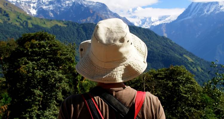 Un excursionista con un sombrero de ala ancha frente a un exuberante paisaje verde y montañoso.