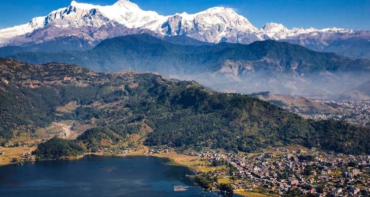 Pintoresca vista de un lago con una vibrante ciudad y majestuosas montañas como telón de fondo.