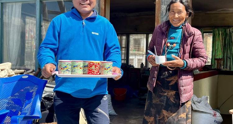 Un anfitrión ofrece tazas en una bandeja mientras una mujer mayor sonríe a su lado en una cabaña rústica de montaña.