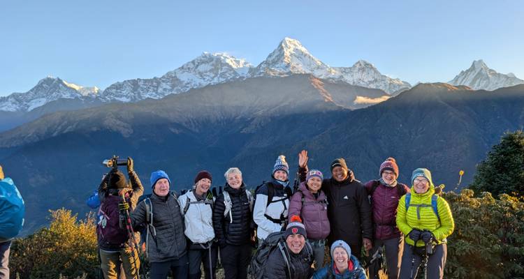 Un grupo de trekking alegre posa al amanecer con la cordillera del Annapurna cubierta de nieve brillando detrás.