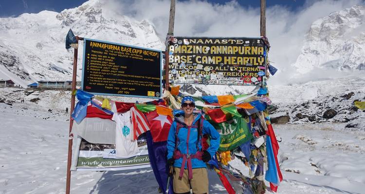 Una persona de pie en el Campo Base del Annapurna con banderas de oración al fondo.