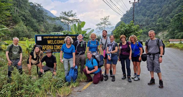 Eine große Trekkinggruppe posiert neben einem Willkommensschild auf einer Bergstraße am Eingang des Annapurna.