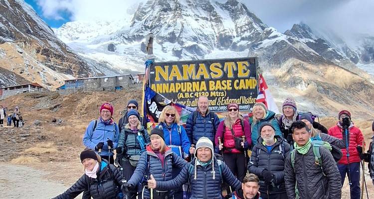 Glückliche Trekker versammeln sich am Namaste Annapurna Base Camp Schild unter verschneiten Gipfeln.