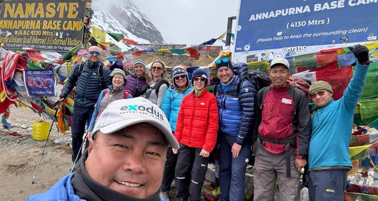 Ein Selfie mit Trekkern und Gebetsfahnen beim Annapurna Base Camp Schild erzeugt eine lebendige Atmosphäre.