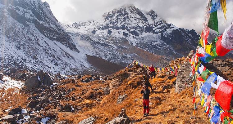 Excursionistas con coloridas banderas de oración, frente a imponentes picos nevados.