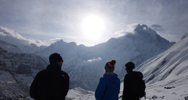 Senderistas en un paisaje nevado con el sol oculto tras un pico.