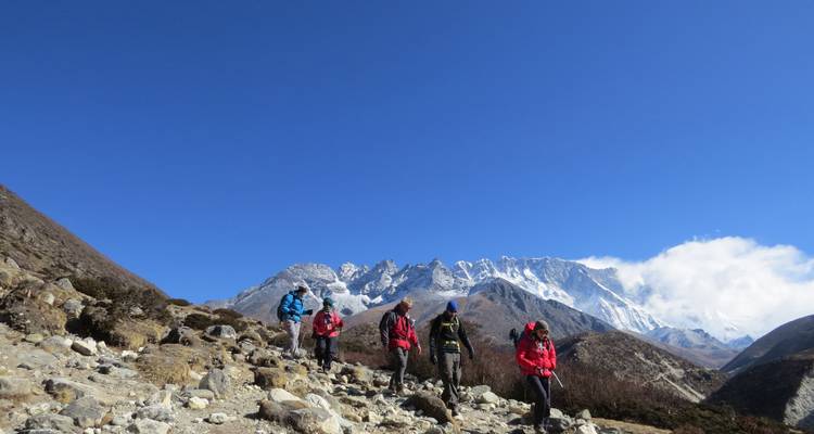 Randonneurs marchant sur un sentier rocailleux avec des sommets enneigés en arrière-plan.