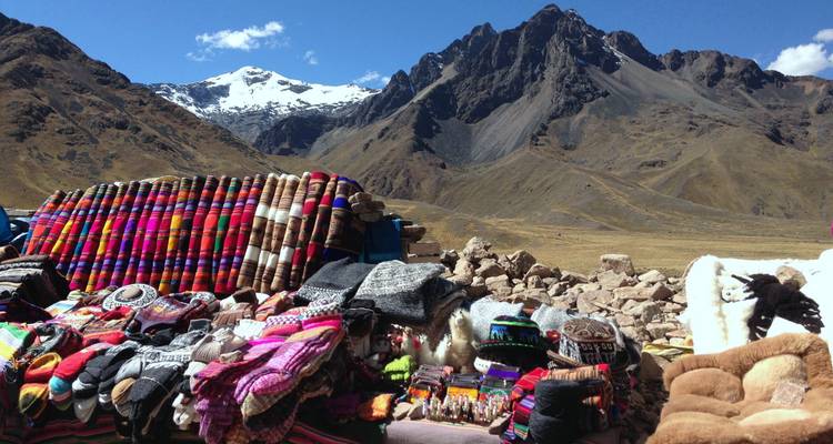 Fondo montañoso con textiles y artesanía locales expuestos.