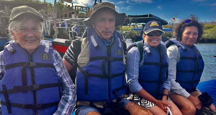 Vier passagiers in reddingsvesten glimlachen aan boord van een opblaasbare boot, klaar voor een Galápagos-excursie.