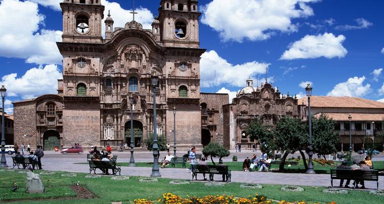 Catedral y feligreses sentados en bancos alrededor de una plaza.