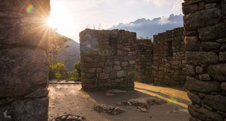 Steinmauern alter Inkaruinen, beleuchtet von tiefem Sonnenlicht mit Andengipfeln im Hintergrund.