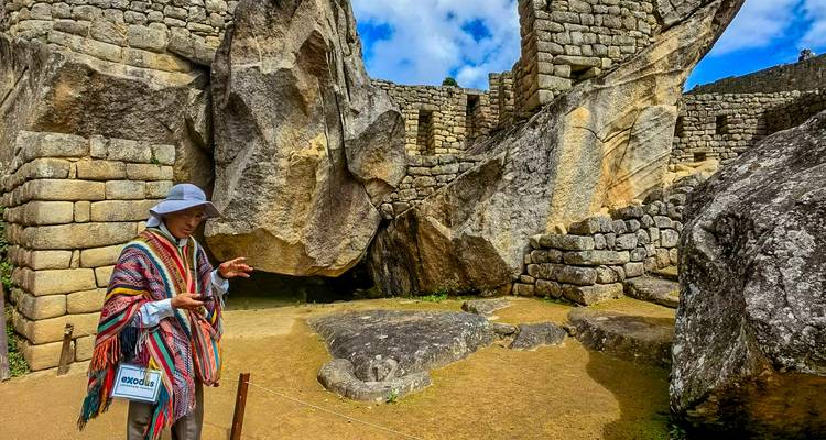 A guide in colorful poncho explains stone ruins within an ancient Inca site.