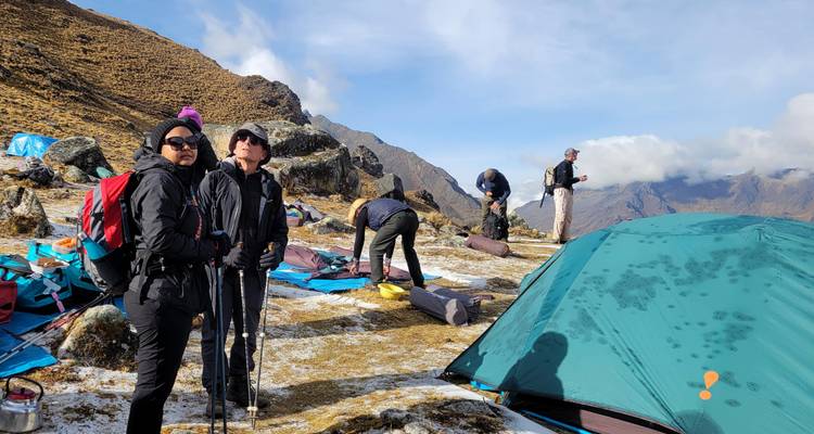 Campers pack gear on a frosty high-altitude campsite beside a teal tent.