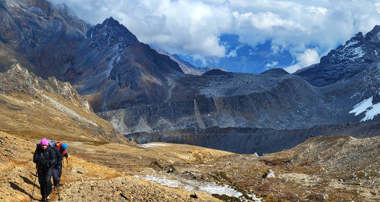 Hikers tackle a barren, high-altitude trail with dramatic ridges and shifting clouds ahead.
