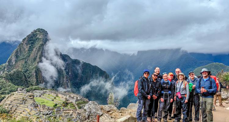 A trekking group poses with misty Machu Picchu ruins and steep peaks behind.