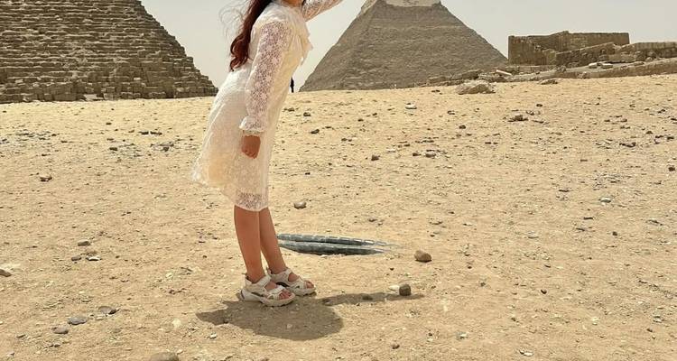 Una persona en un vestido blanco posando frente a dos pirámides en un entorno desértico.