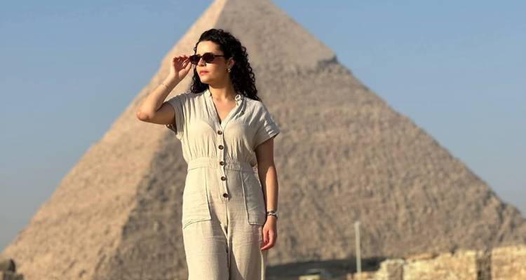 Una persona con gafas de sol posando frente a una pirámide.