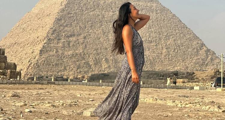 Una persona con un vestido suelto con una pirámide al fondo.