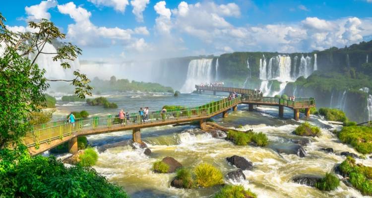 Ein malerischer Blick auf die Iguazu-Wasserfälle mit einem Steg und Touristen.