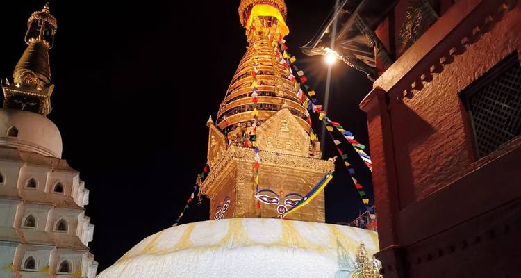 Vue extérieure d'un stupa doré la nuit avec des drapeaux colorés.