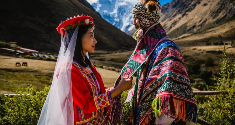 Pareja en colorido atuendo de boda andino se miran el uno al otro con el pico nevado de Salkantay detrás.