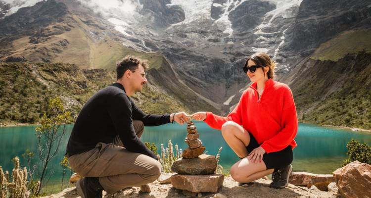 Una pareja comparte un momento junto a piedras apiladas contemplando el vibrante lago azul Humantay.
