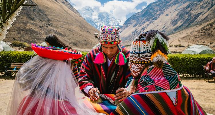 Ceremonia chamánica andina tradicional con textiles vibrantes y picos nevados al fondo.