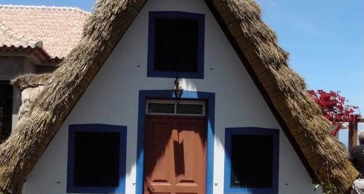 Pequeña casa en forma de A con tejado de paja bajo un cielo azul.